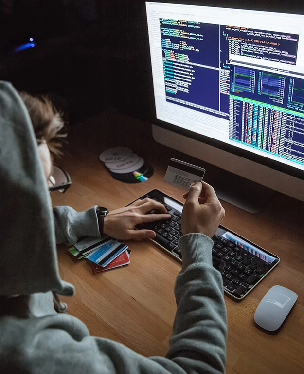 Ein Mann sitzt vor einem Computer, tippt mit einer Hand auf die Tastatur und mit der anderen Hand hält er eine Kreditkarte