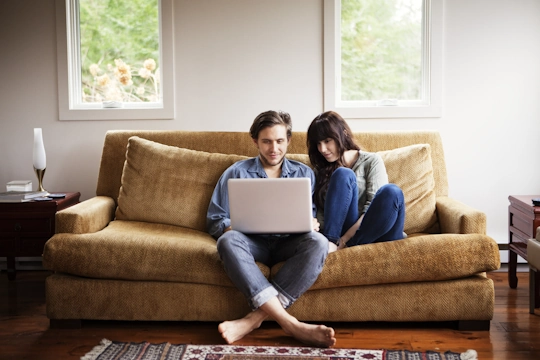 Ein junges Paar sitzt auf der Couch vor dem Laptop