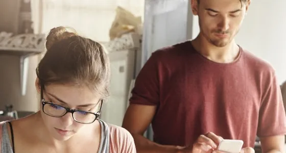 Frau im Vordergrund, Mann im Hintergrund spielt auf dem Handy