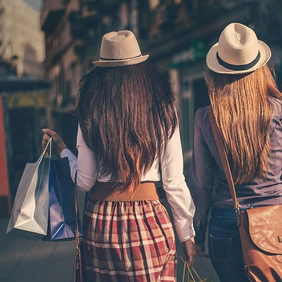 Zwei Frauen von hinten mit Hüten am Kopf und Einkaufstaschen