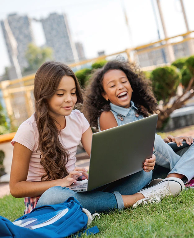 3 Kinder sitzen in der Wiese mit einem Laptop