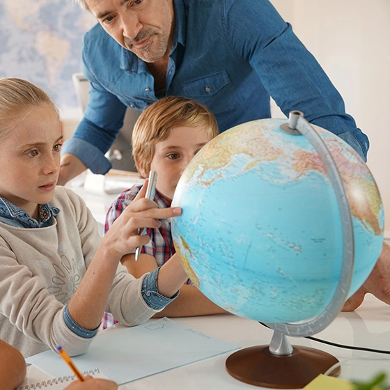 Ein Mann zeigt Kindern etwas auf einem Globus