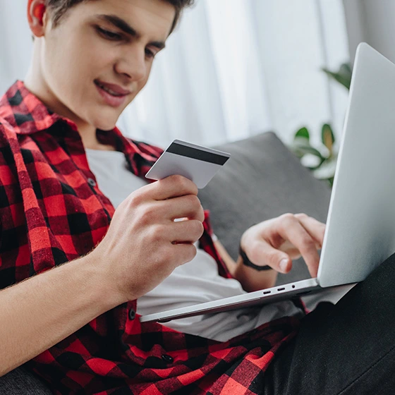 Ein Jugendlicher mit Kreditkarte in der Hand vor dem Laptop