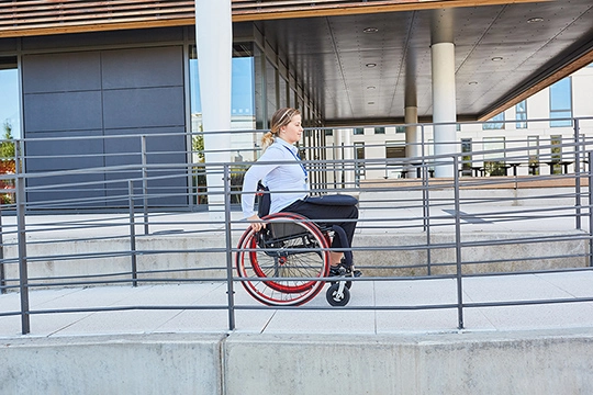 Eine Frau fährt mit dem Rollstuhl eine Betonrampe hinauf