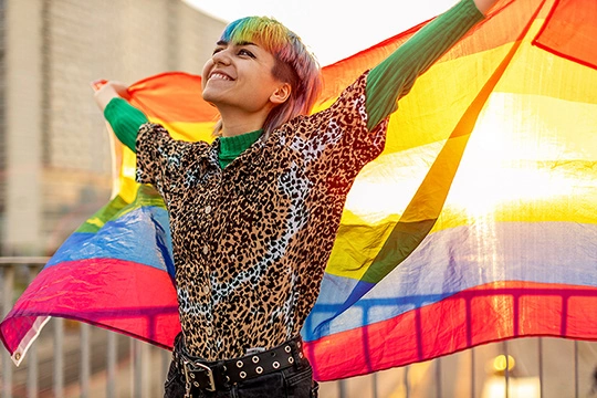 Eine junge Frau mit bunten Haaren hält eine Regenbogenfahne in die Höhe