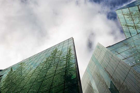 Hochhäuser aus Glas in denen sich die grünen Bäume spiegeln werden von unten fotografiert