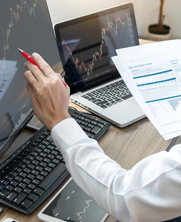 Ein Mann  mit Unterlagen in der Hand vor dem Computerbildschirm