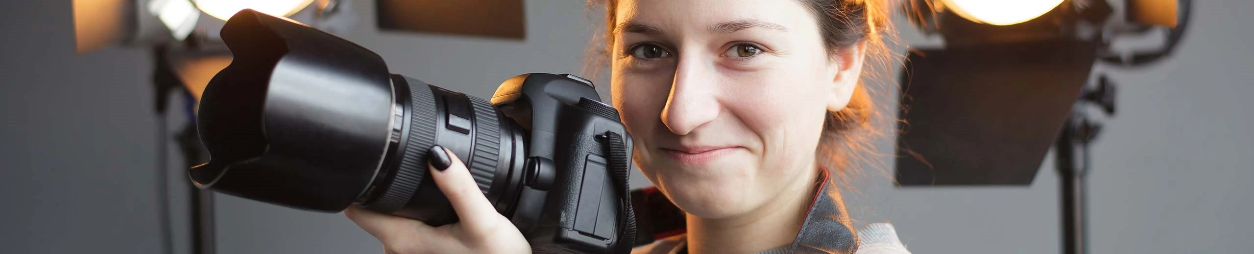 Junge Frau lächelt in die Kamera und hält selbst einen Fotoapparat in der Hand