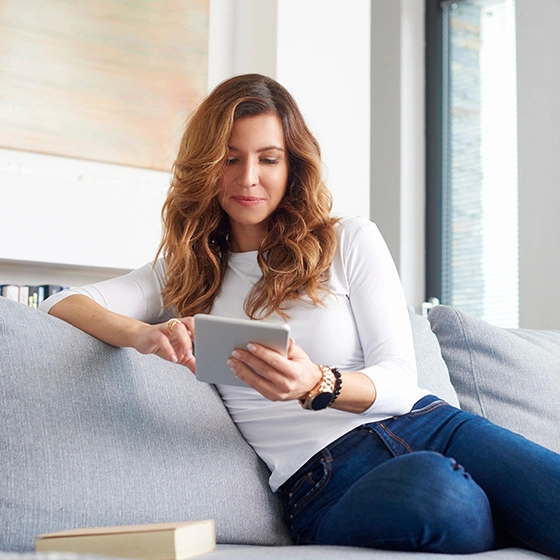 Frau mit Tablet in der Hand sitzt auf Couch